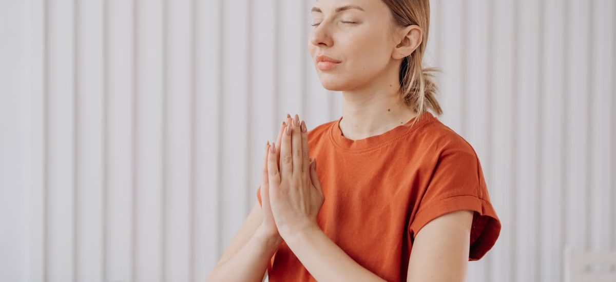 A woman in orange practices meditation indoors, expressing mindfulness and concentration.